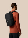 Profile view of a man wearing a gunmetal Castore Core Backpack over an orange shirt