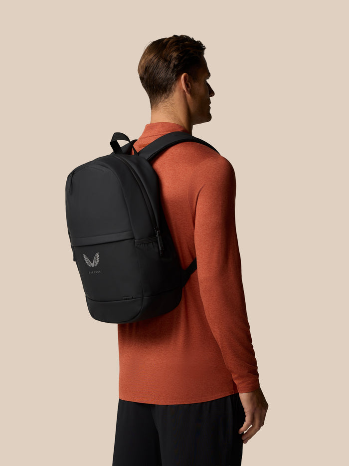 Profile view of a man wearing a gunmetal Castore Core Backpack over an orange shirt