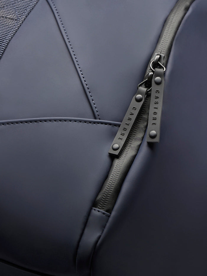 Close-up of navy Core Holdall zipper area with dual pulls bearing CASTORE on dark PU fabric.