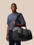 Unisex Core Holdall carried over the shoulder by a man in a blue shirt against a beige backdrop