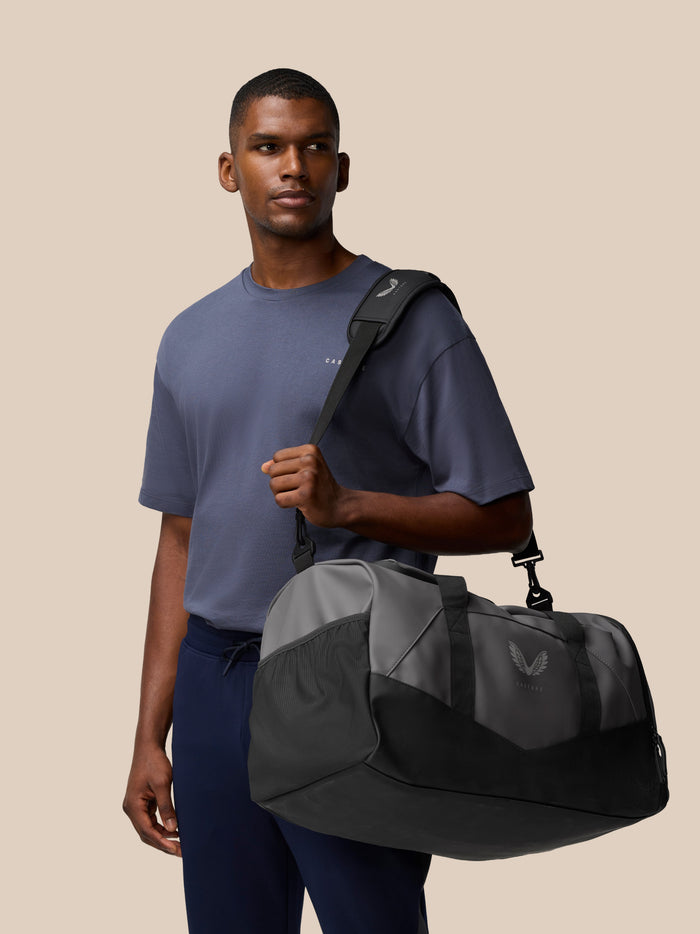 Unisex Core Holdall carried over the shoulder by a man in a blue shirt against a beige backdrop