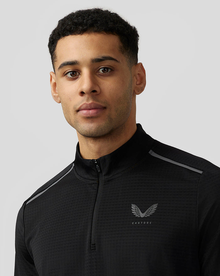 Close up of model in black Apex Aeromesh Top with funnel neck and reflective Castore branding on the left chest and shoulder piping.
