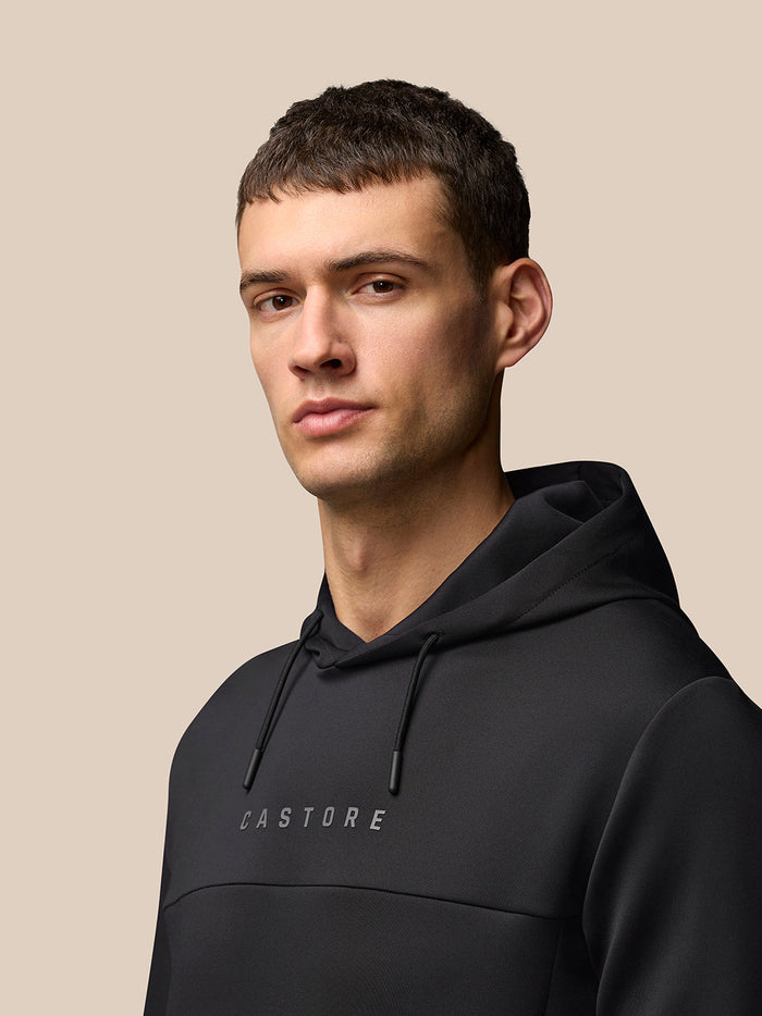 Portrait of a man in a black Flex Hoodie with hood up against a beige background