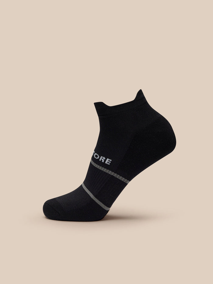 Black ankle sock from a 3 pack with Castore branding and a light gray cuff stripe, shown on a beige background.