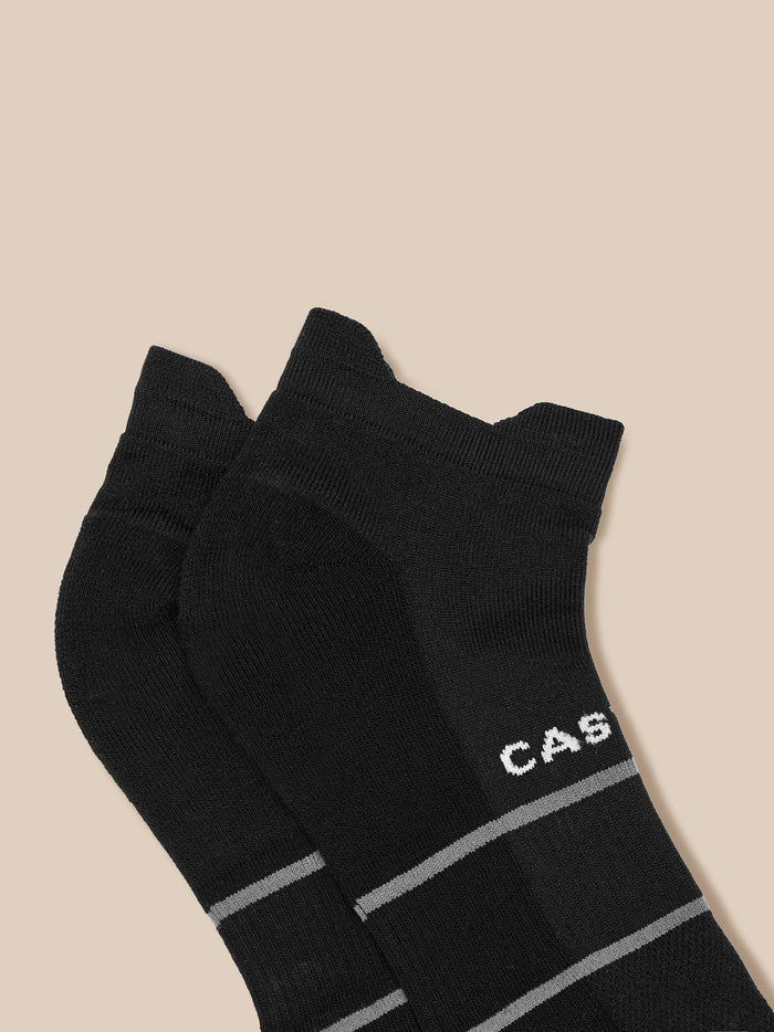 Two black ankle socks with Castore lettering and gray stripes laid on a beige backdrop.