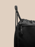 Close up of a black Castore gym bag with braided drawstrings and a zippered pocket on textured fabric