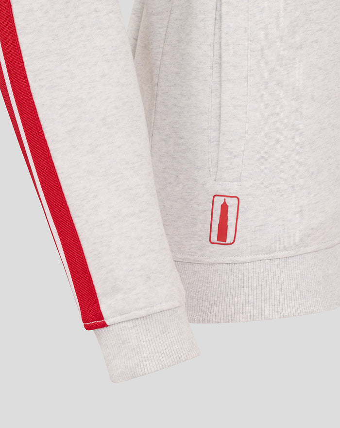 Hem area of the grey hoodie with a red stripe along the sleeve and a small red patch near the hem.