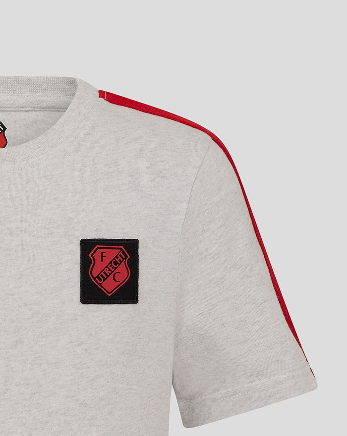 Close up of the left chest black patch with the FC Utrecht crest on a light grey junior T-shirt with red shoulder piping.