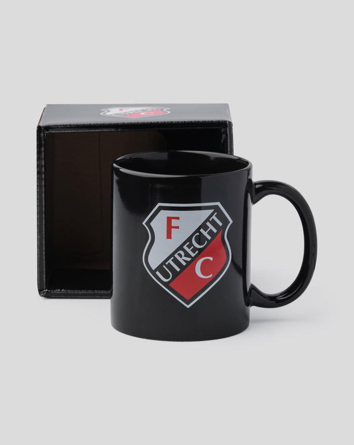 Front view of a black FC Utrecht mug with shield logo, partially inside a black box.