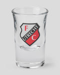 Close up of a clear FC Utrecht shot glass featuring the crest.